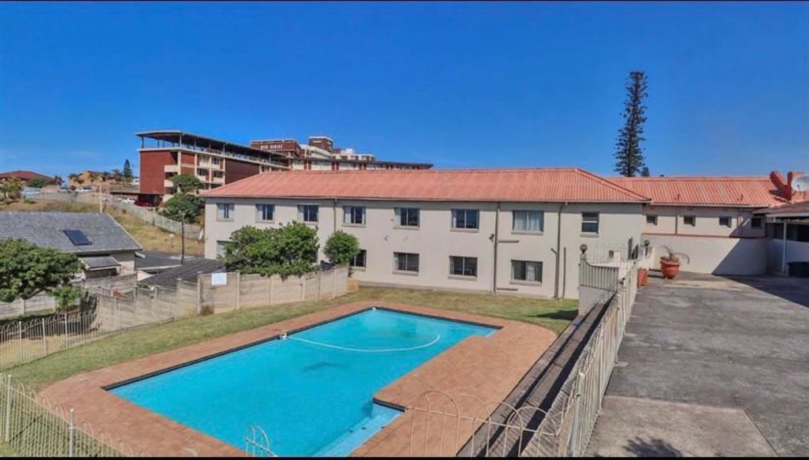 Tetelestai Recovery Centre fenced swimming pool with a paved surround, lawn area, and the residential accommodation block in the background